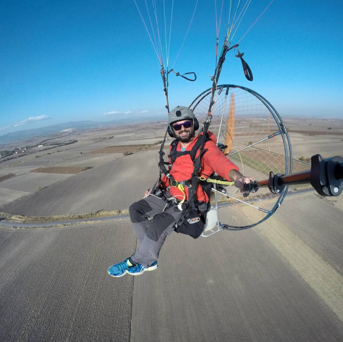 Paramotor pilot selfie shot flying over brown fields.