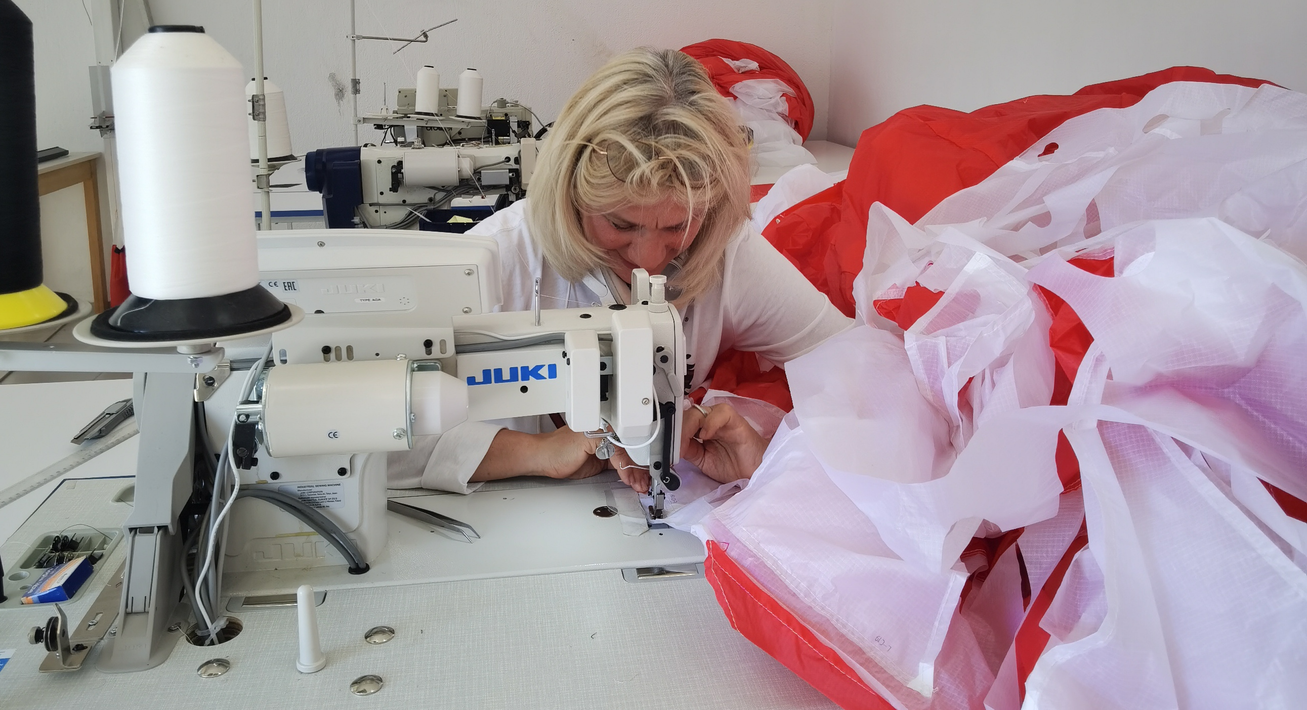 Repairing red and white paraglider with a sewing machine.